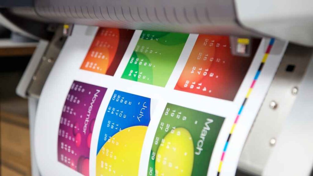 A Multicolored Calender print coming out the the DTF printer representing the query:DTF vs Sublimation. What is the difference between dtf and sublimation ?