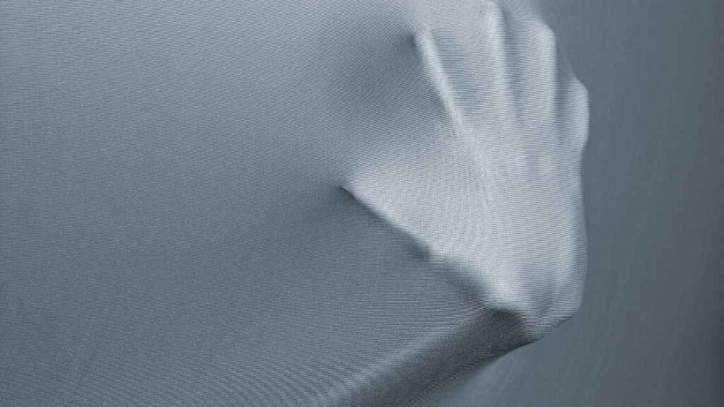 A person's hand stretching the spandex alike fabric from behind representing the query: Is Nylon Stretchy? Or Is nylon stretchable? Or Is nylon stretchy? Or Can you stretch nylon? Or How to stretch nylon?