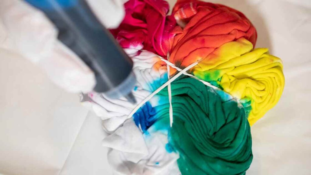 A person tie dyeing microfibers fabric with blue ink representing the query: Can you tie dye microfibers? Or Can you dye microfiber? Or Is tie dyeing microfibers possible ? Or How to tie dye microfibers?