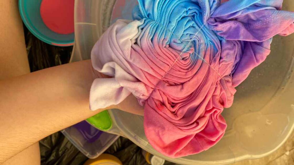 A person putting tie dyed fabric into water representing the query: Can you tie dye microfibers? Or Can you dye microfiber? Or Is tie dyeing microfibers possible ? Or How to tie dye microfibers?
