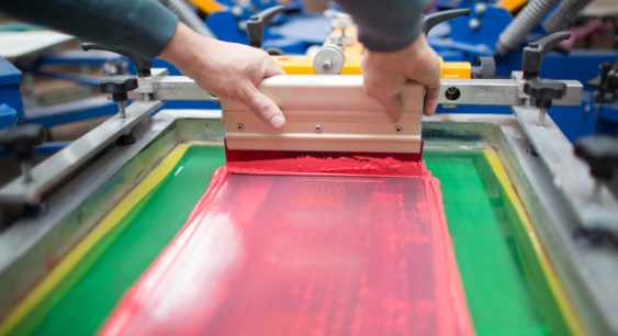 A person Screen printing on the fabric with red color representing the queries: What is Screen Printing? What are Types of Screen Printing? What is the Process of Screen printing ?