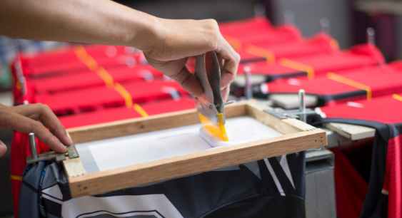 A person printing on shirt through screen printing method representing the queries: Types of shirt printing Or Types of t shirt printing Or Different Types of Shirt printing Or Types of printing on shirt Or Different Types of t shirt printing Or Different types of tshirt printing.