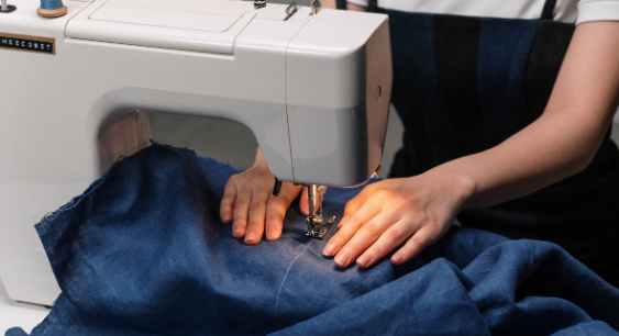 A person using sewing machine sew a blue colored fabric representing the queries: How to fix cracked print on a shirt?