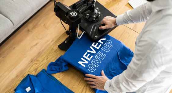 A person printing a design onto a blue t shirt with heat press representing the queries: How to put a picture on a shirt? Or How to Put Pictures on a shirt? How to Put a Picture on a shirt with cricut ? Or How to Put a picture on a shirt at home? Or How to put any picture on a shirt? Or How to put an image on a shirt? How to put picture on shirt ? Or How to put a picture on a tshirt? Or How to put an image on a shirt?